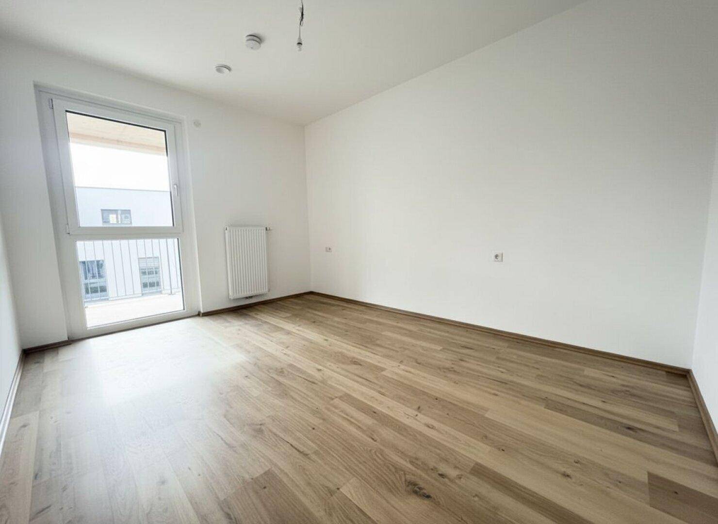 Helles Schlafzimmer mit Laminatboden und Zugang zu einem französischen Balkon.