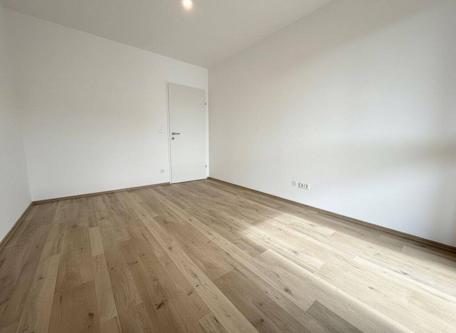 Leeres Zimmer mit Laminatboden und weiß gestrichenen Wänden, ideal als Schlafzimmer.