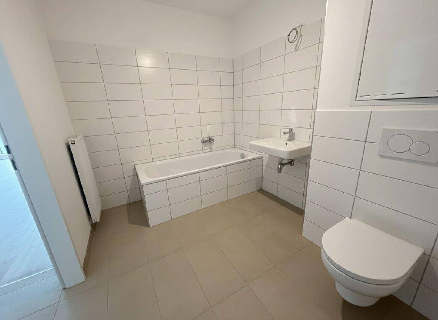 Helles Badezimmer mit Badewanne, WC und Waschbecken, ausgestattet mit weißen Fliesen.