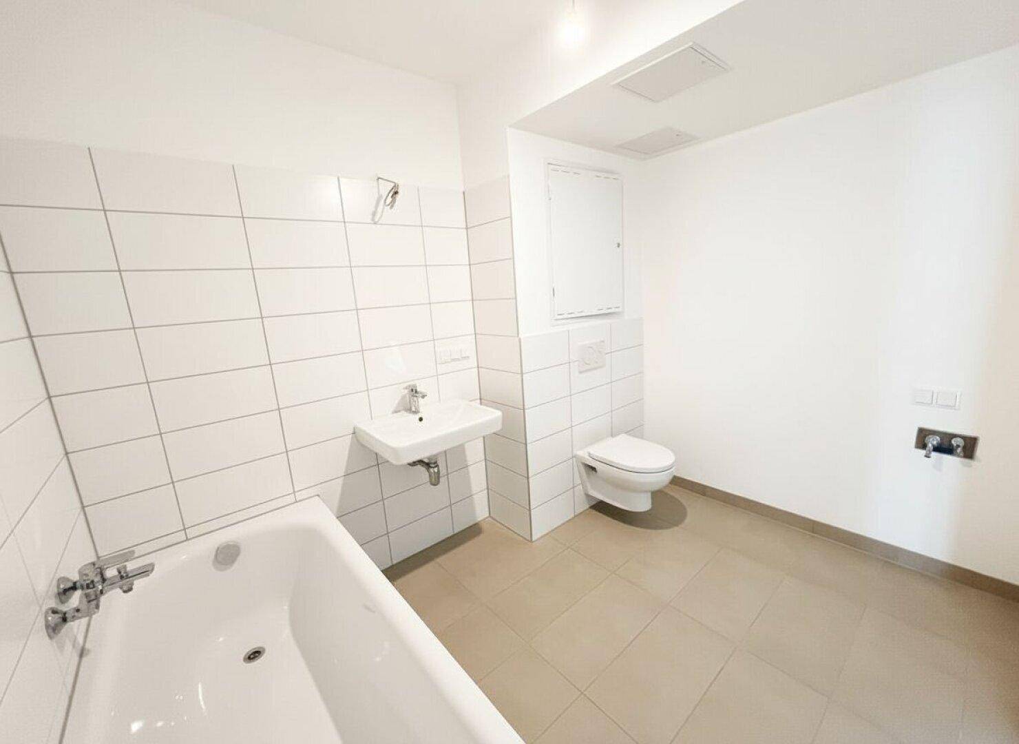 Modernes Badezimmer mit Badewanne, WC und Waschbecken, hell gefliest.