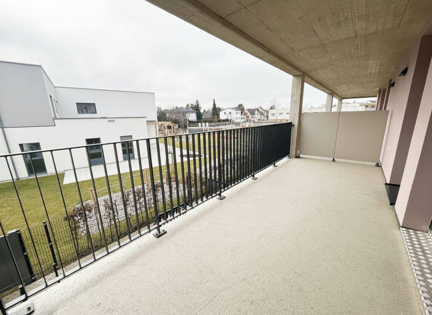 Breiter Balkon mit Blick auf die grüne Umgebung und weitere Wohngebäude.