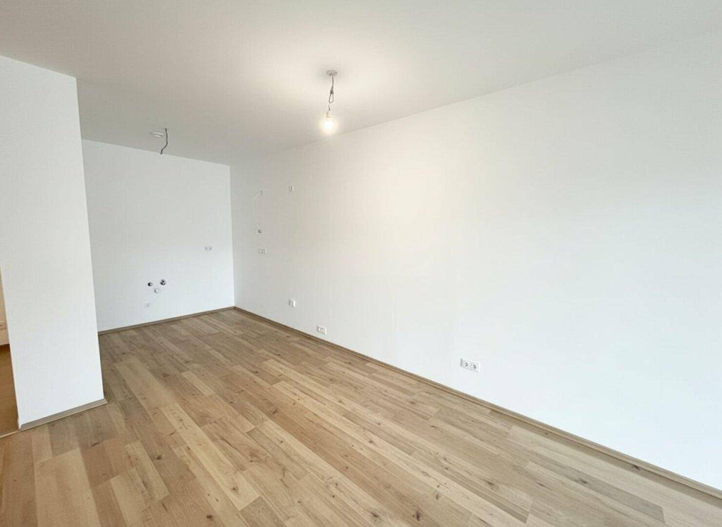Sauberer, leerer Wohnbereich mit hellem Laminatboden und weißen Wänden.