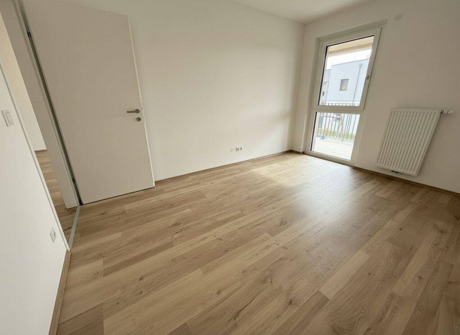 Unmöbliertes Schlafzimmer mit Laminatboden und großem Fenster mit Blick nach draußen.
