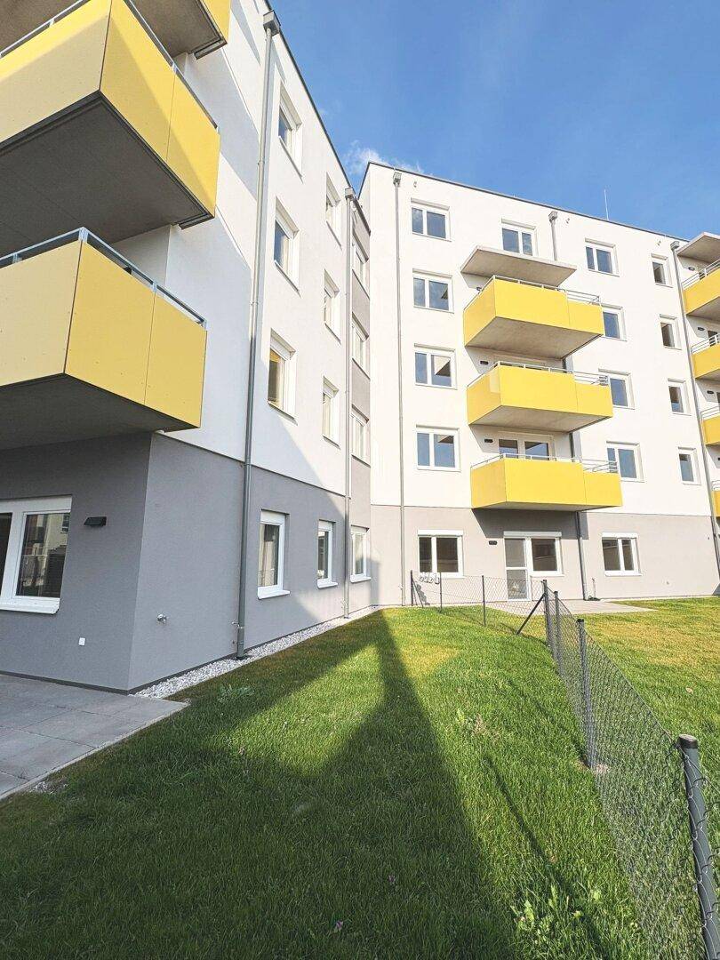 Moderne Wohngebäude mit weißer und grauer Fassade sowie gelben Balkonen unter blauem Himmel.