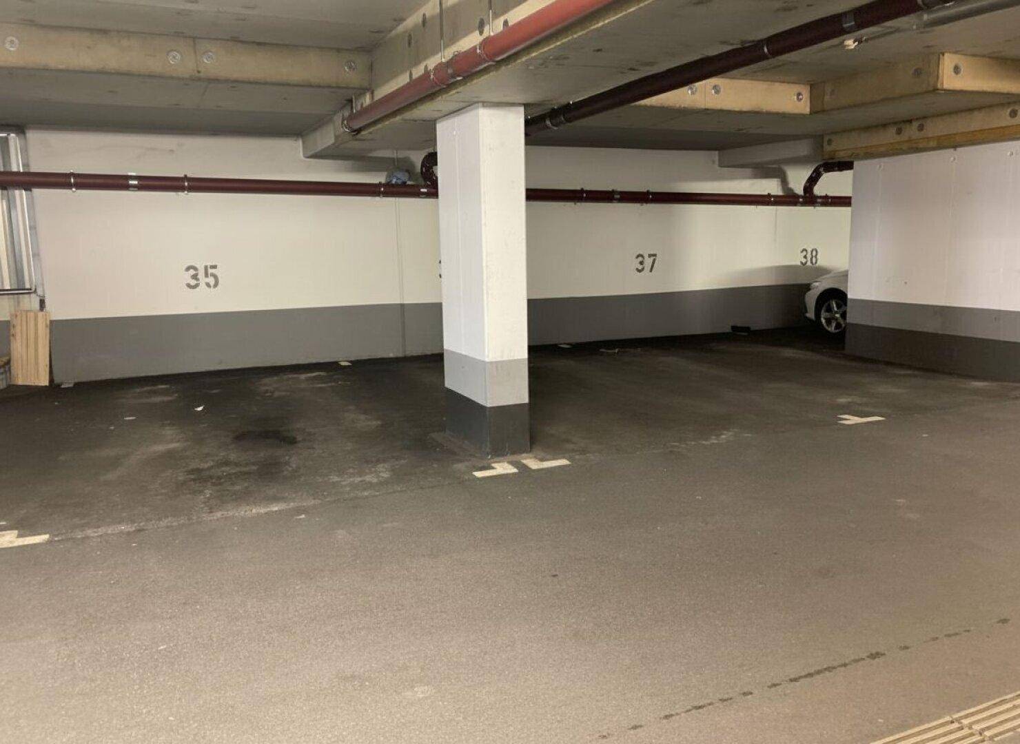 Innenbereich der Tiefgarage mit nummerierten Stellplätzen und Betonstützen, ein Fahrzeug ist sichtbar.