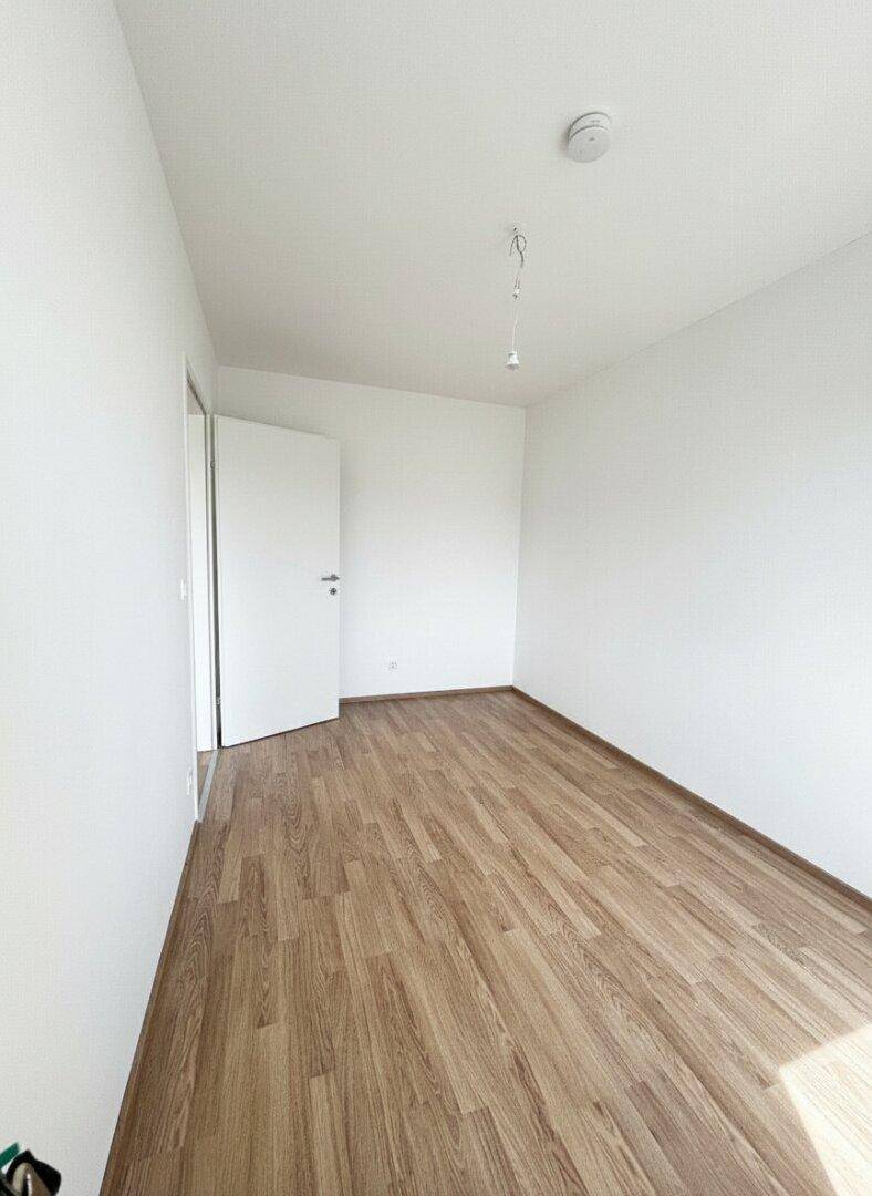 Helles Schlafzimmer mit Laminatboden und weiß gestrichenen Wänden, ideal für individuelle Einrichtung.