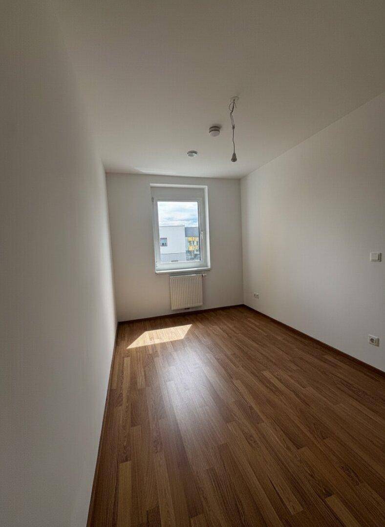 Sonniger Raum mit Laminatboden und einem Fenster, das viel Tageslicht hereinlässt.