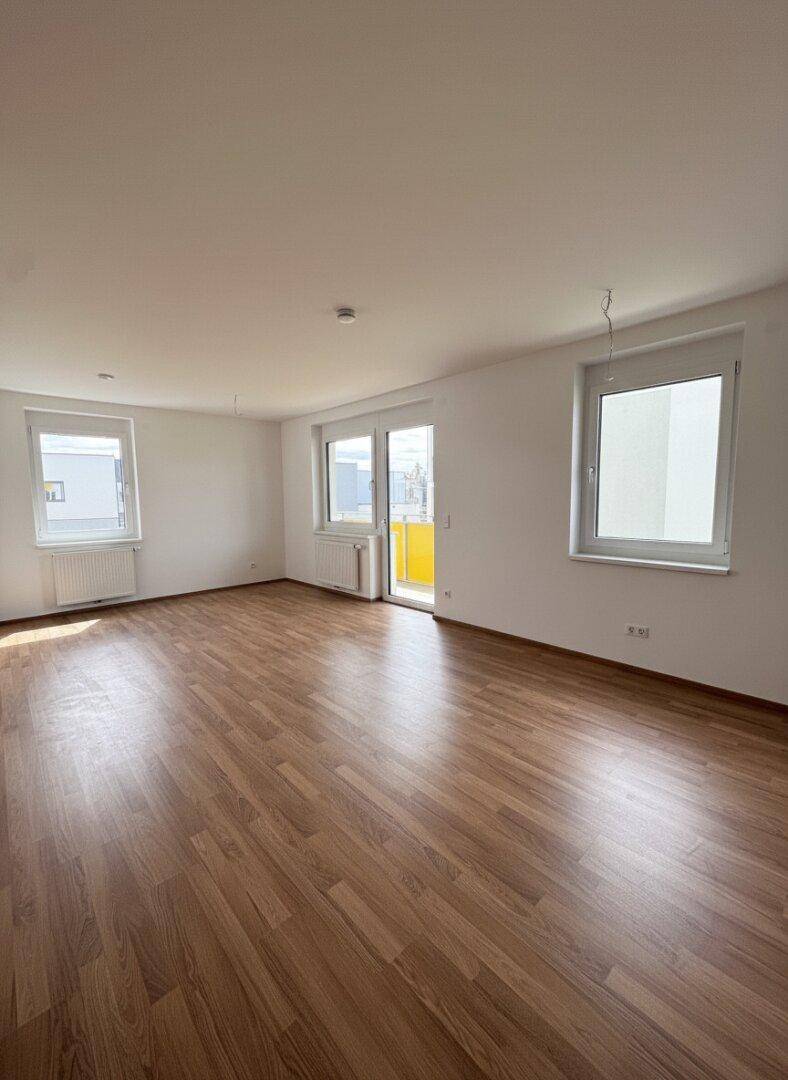Geräumiges Wohnzimmer mit Laminatboden, großen Fenstern und direktem Zugang zum Balkon.