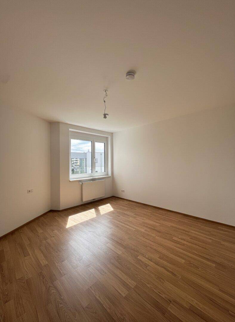 Lichtdurchflutetes Zimmer mit Laminatboden und einem großen Fenster, perfekt für ein Schlafzimmer.