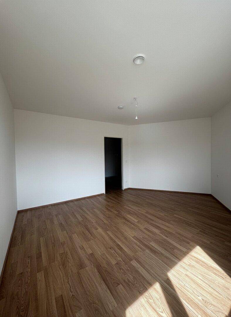 Geräumiger, leerer Raum mit Laminatboden und weiß gestrichenen Wänden, ideal für individuelle Gestaltung.