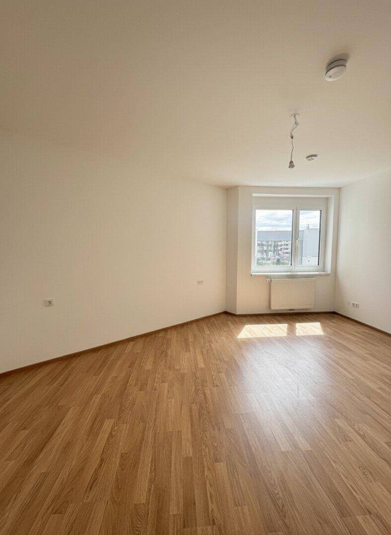 Heller Raum mit Laminatboden und einem Fenster, das viel Sonnenlicht hereinlässt.