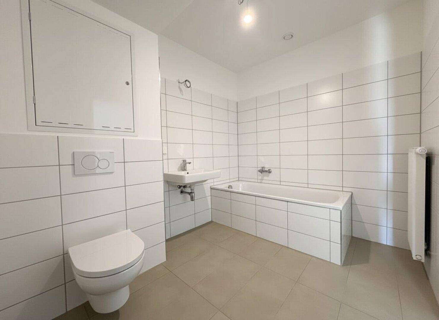 Modernes Badezimmer mit Badewanne, WC und Waschbecken, hell gefliest und funktional gestaltet.