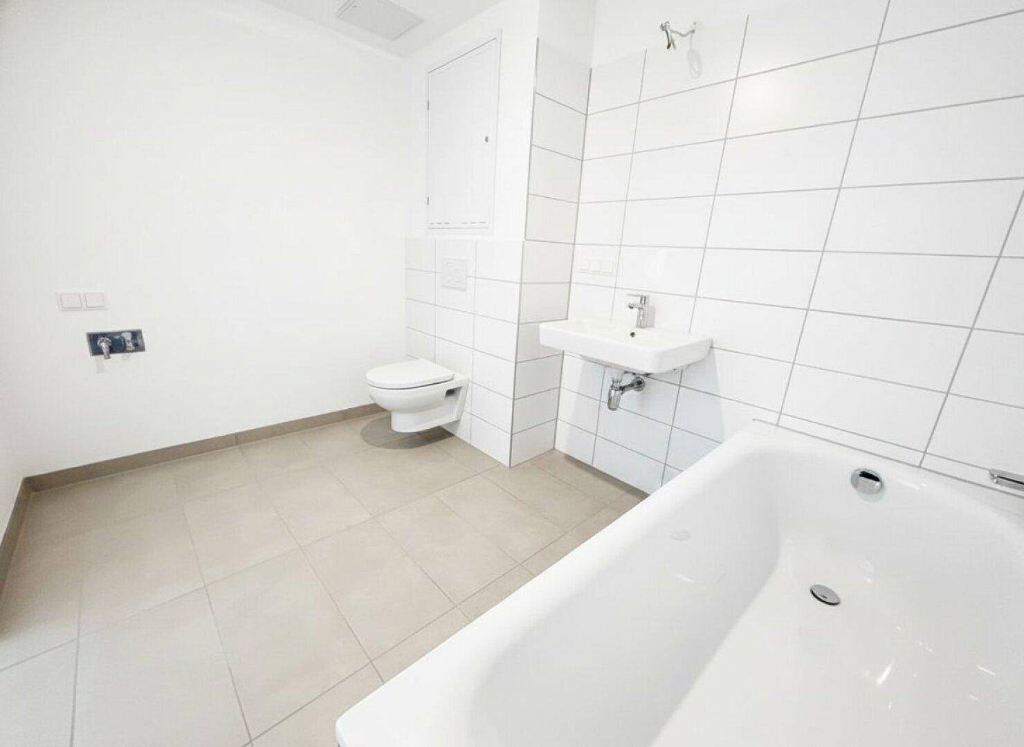 Helles Badezimmer mit Badewanne, WC und Waschbecken, in neutralen Farben gefliest und pflegeleicht.