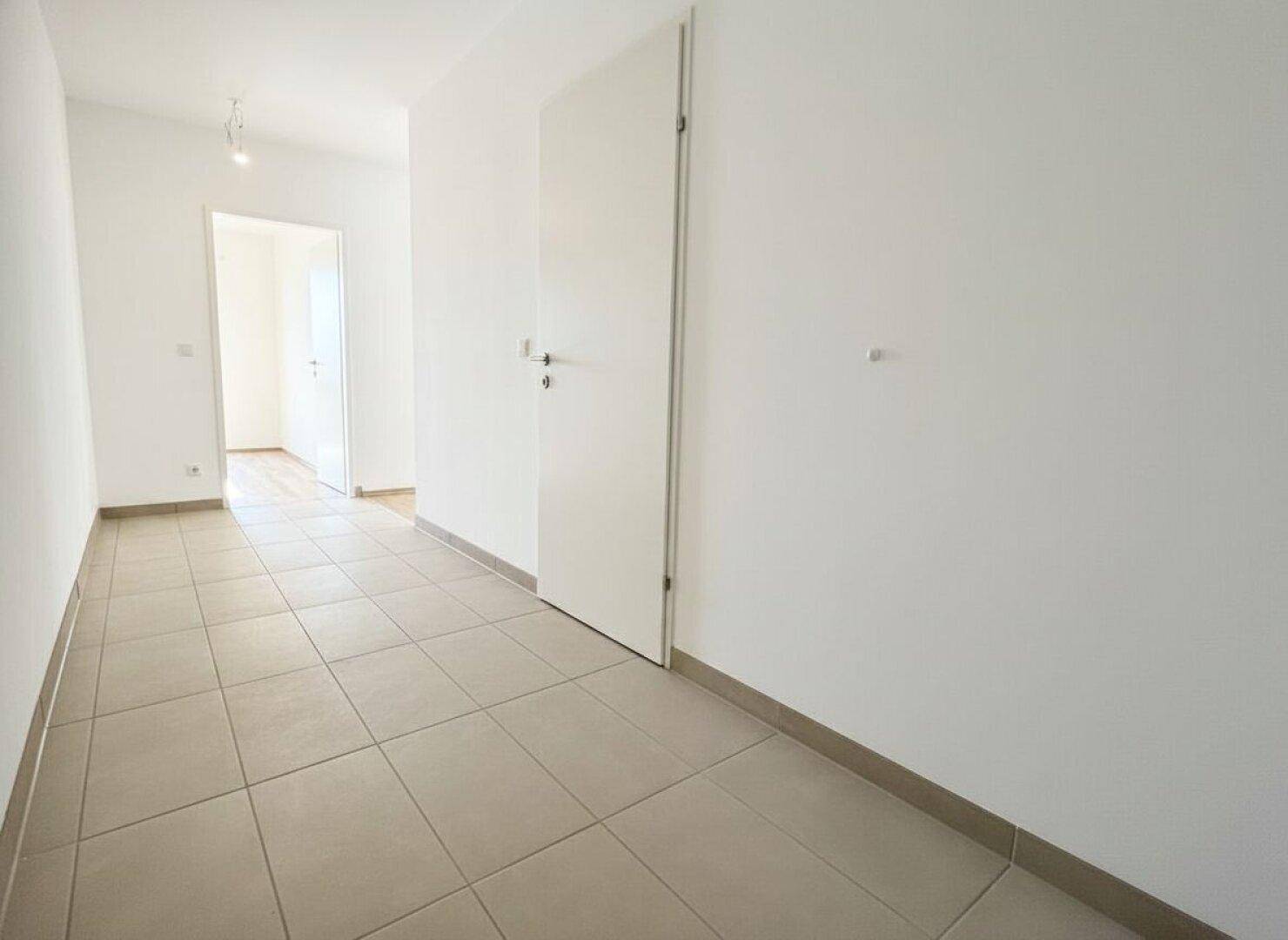 Geräumiger Flur mit Fliesenboden und weißen Wänden, führt zu den Wohnbereichen der Wohnung.