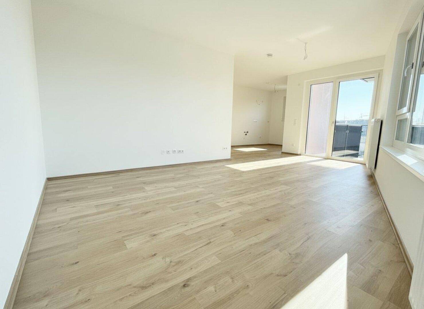 Geräumiger, heller Wohnbereich mit Holzboden und Zugang zu einem Balkon, ideal für offenes Wohnen.
