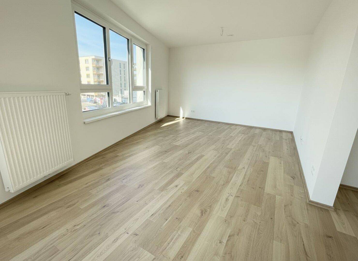 Helles Zimmer mit Holzboden und großem Fenster, ideal als Schlaf- oder Arbeitszimmer in einem Neubau.