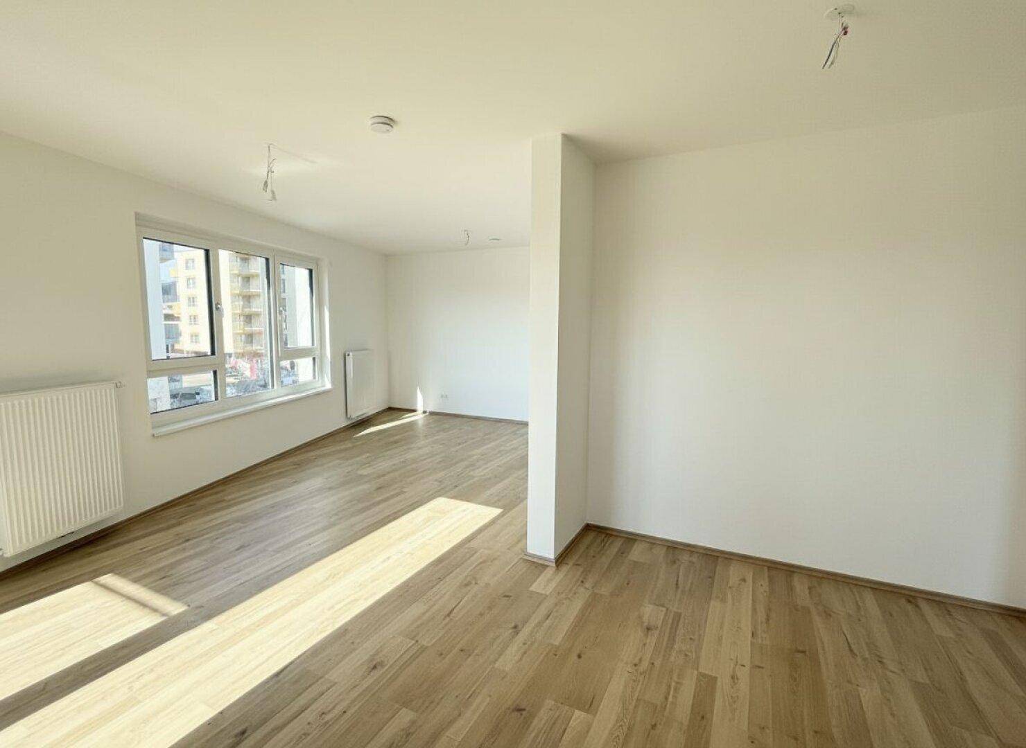 Offener, heller Wohnbereich mit Holzboden und viel Tageslicht durch große Fenster, modern und einladend.