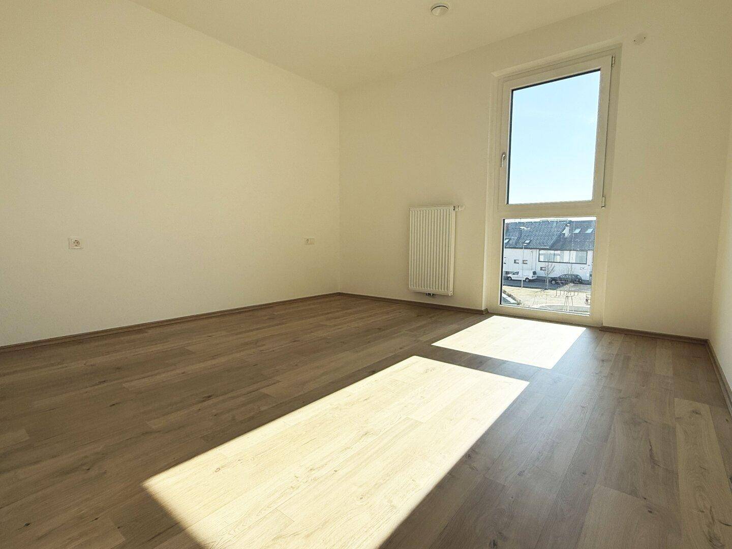 Helles Zimmer mit Holzboden und großem Fenster, ideal als Schlaf- oder Kinderzimmer in einem Neubau.