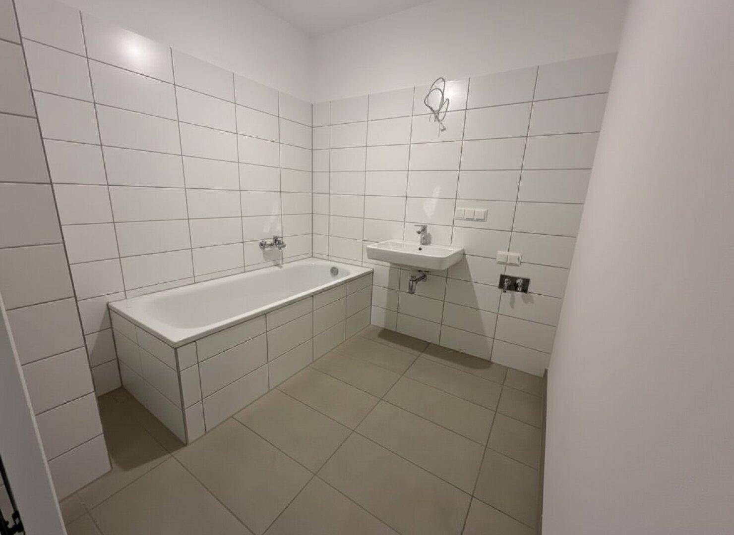 Modernes Badezimmer mit weißen Fliesen, Badewanne und einem einzelnen Waschbecken.