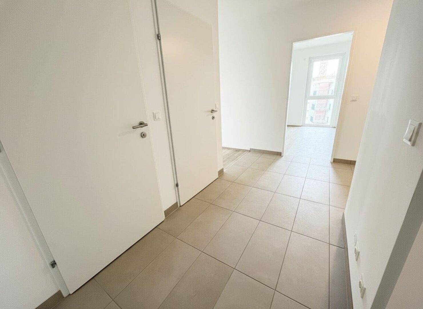 Heller Flur mit modernen grauen Fliesen und weißen Türen, der zu den Wohnräumen führt.