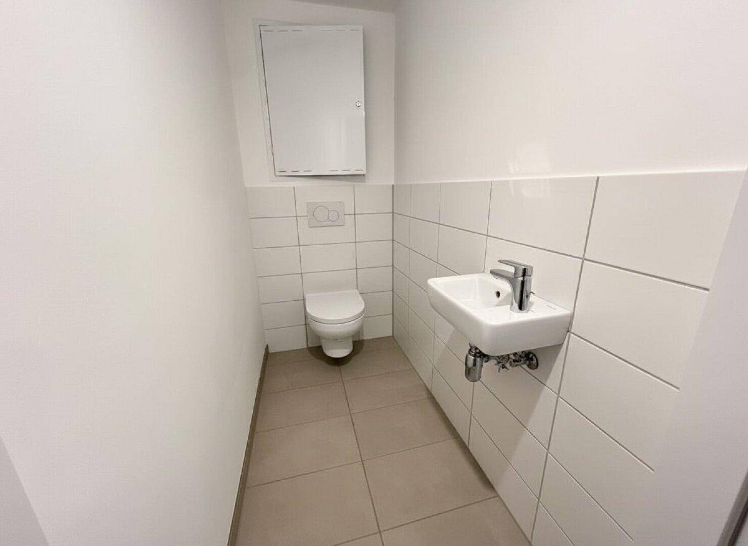 Funktionelles Gäste-WC mit weißen Fliesen, wandhängender Toilette und kleinem Waschbecken.