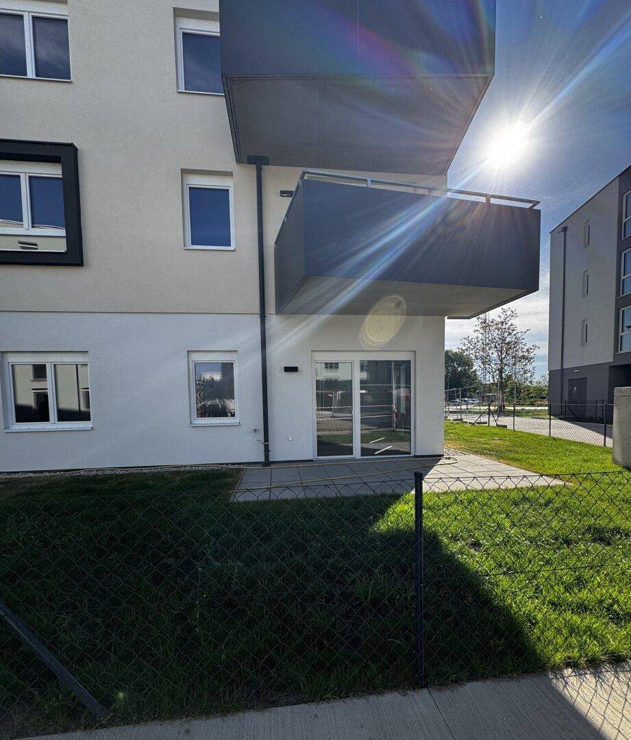 Sonnenbeschienene Fassade eines modernen Wohngebäudes mit dunklen Balkonen und einer Rasenfläche.