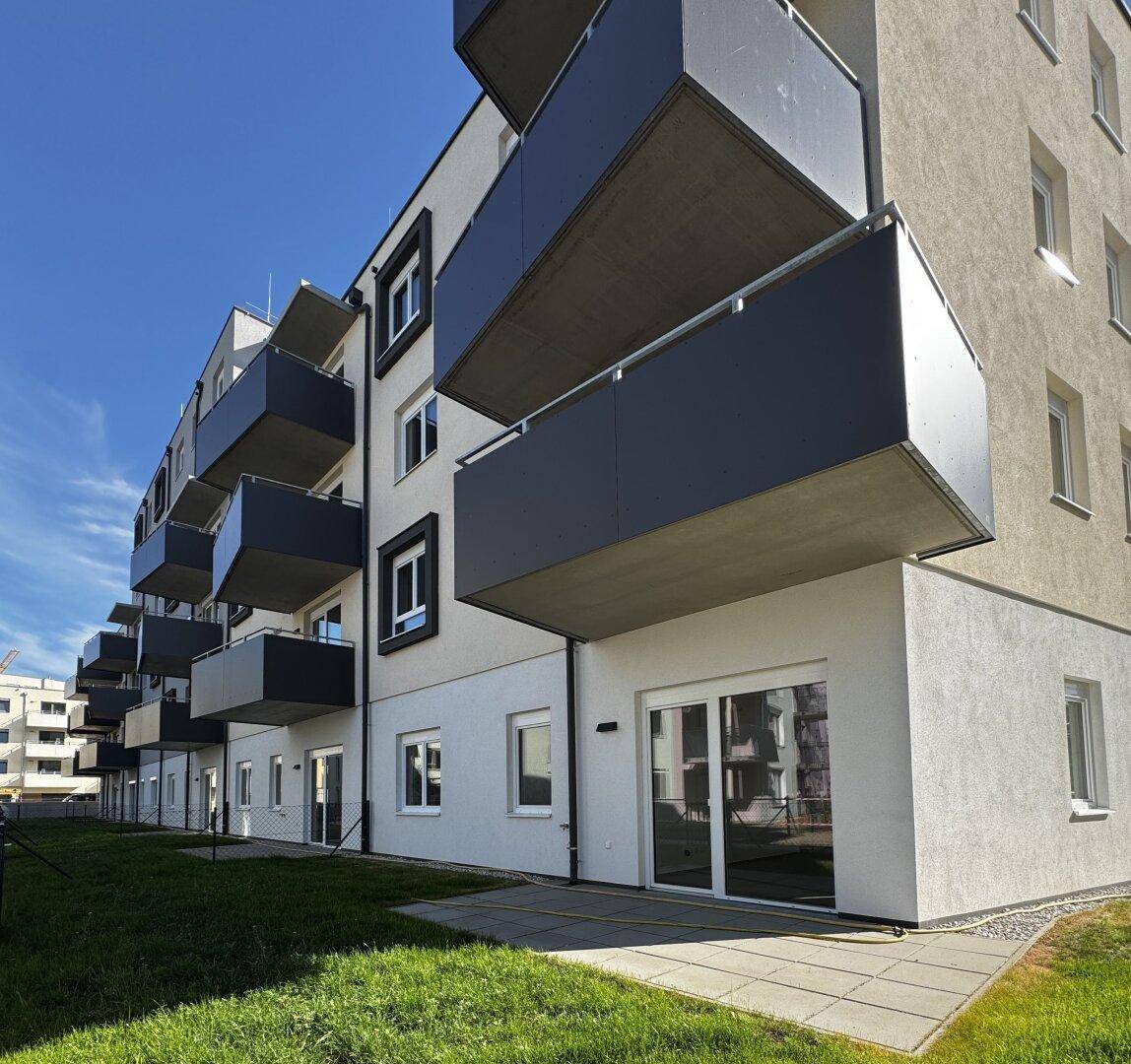 Modernes Wohngebäude mit weißer Fassade, dunklen Balkonen und einer gepflegten Rasenfläche im Vordergrund.