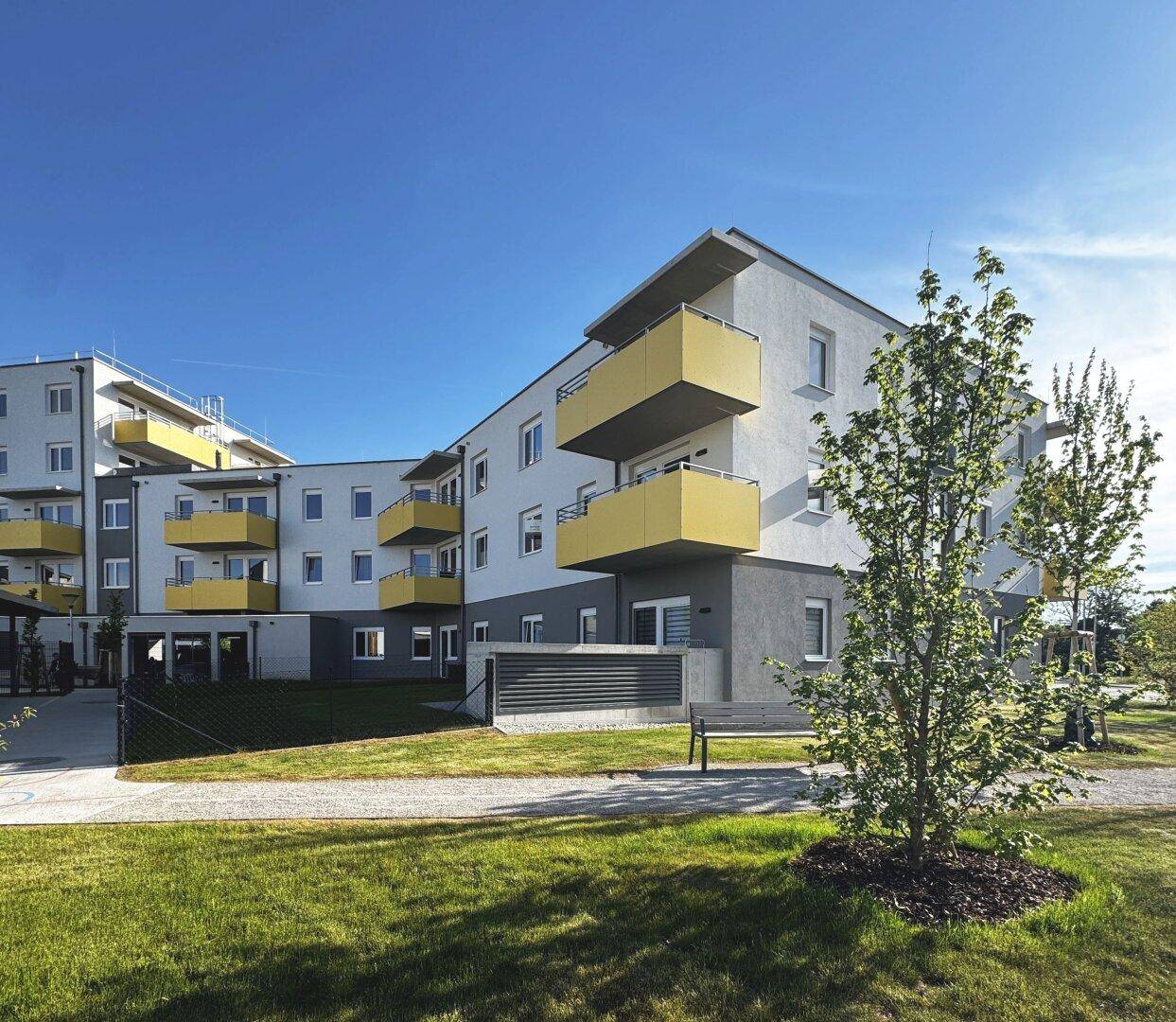 Moderne Wohnanlage mit weißer Fassade, auffälligen gelben Balkonen und gepflegter Rasenfläche.