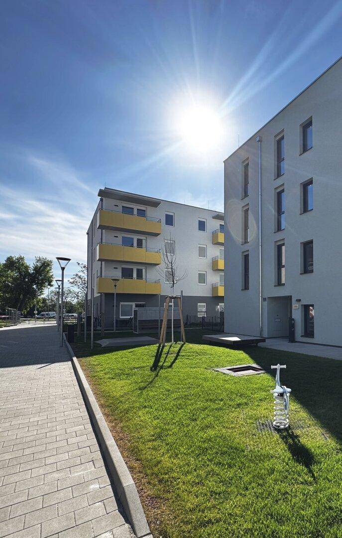 Sonnenbeschienene Fassade eines modernen Wohngebäudes mit gelben Balkonen und einem Gehweg.