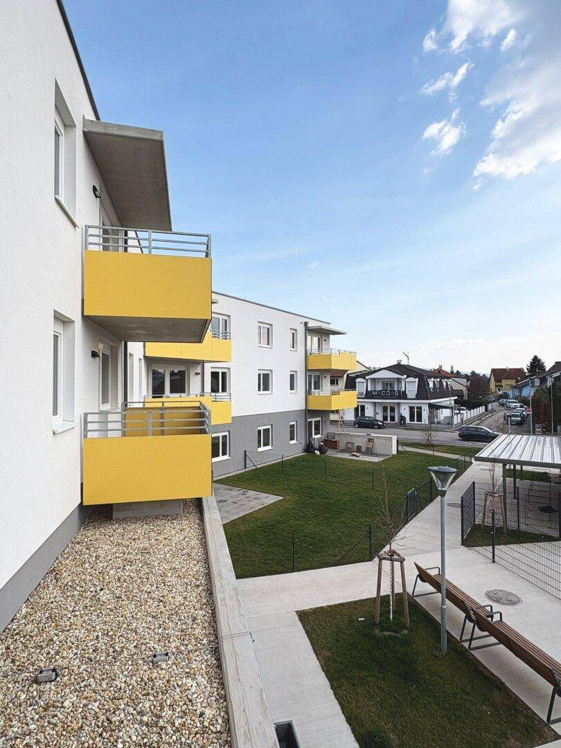 Moderne Wohngebäude mit gelben Balkonen und einem Gemeinschaftsbereich mit Bänken und Grünflächen.
