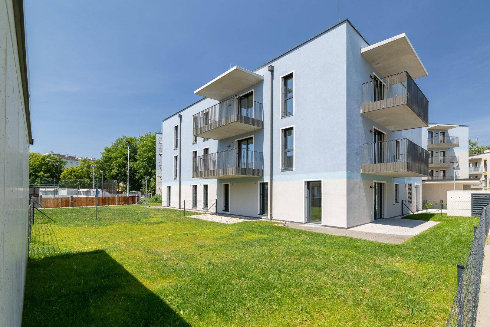 Modernes Wohngebäude mit blauer und weißer Fassade, Balkonen und einer weitläufigen Rasenfläche.