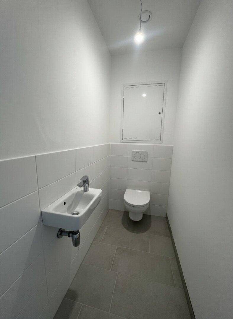 Funktionelles Gäste-WC mit Wand-WC, kleinem Waschbecken und modernen Fliesen.