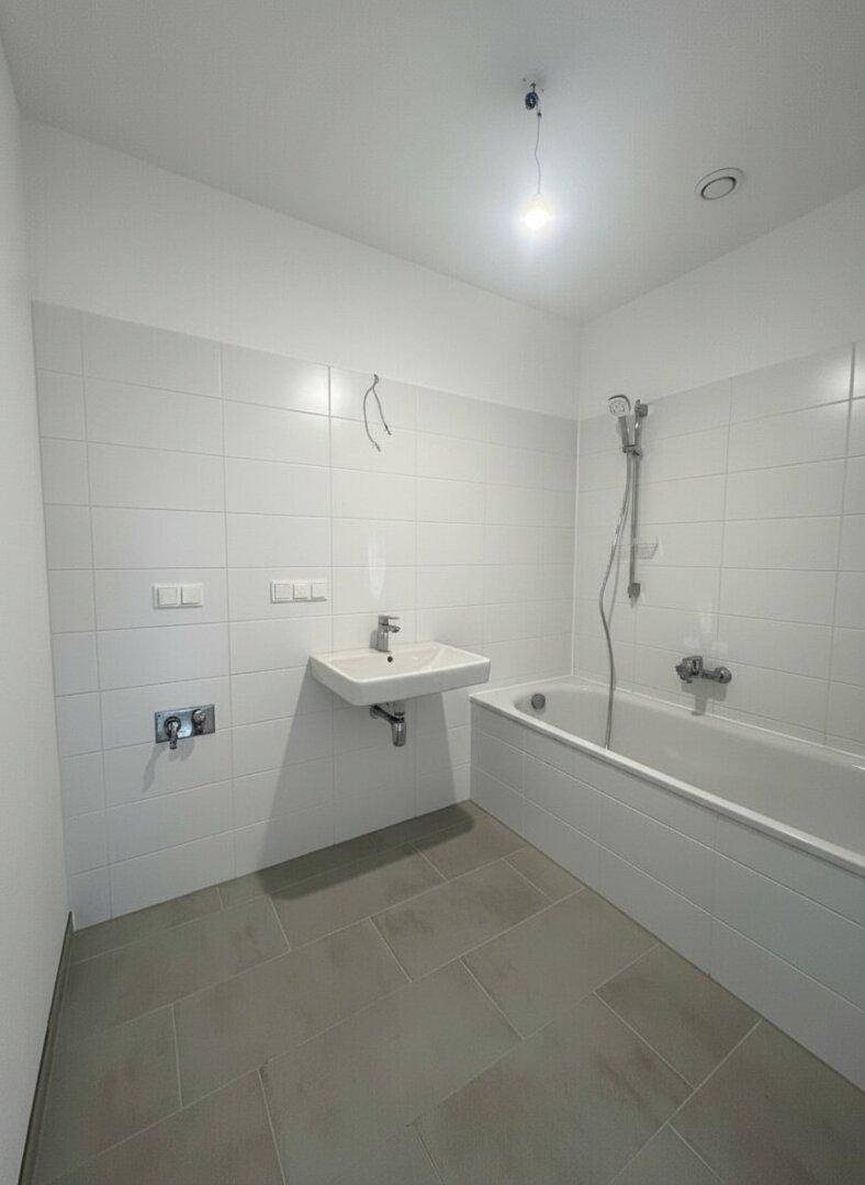 Modernes Badezimmer mit weißen Wandfliesen, grauen Bodenfliesen, Badewanne und Waschbecken.