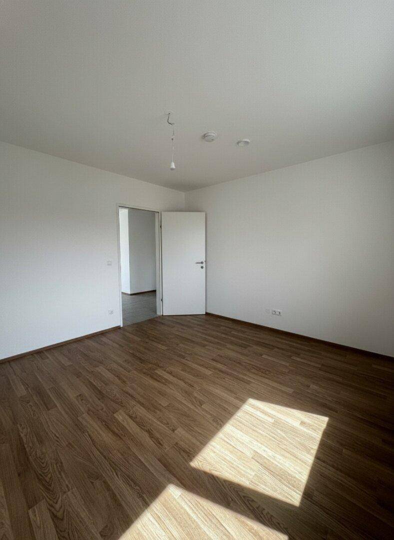 Leeres Zimmer mit Laminatboden und offener Tür, das vielseitig nutzbar ist.