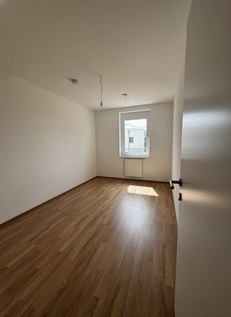Helles, leeres Zimmer mit Laminatboden und einem Fenster, ideal als Schlaf- oder Arbeitszimmer.