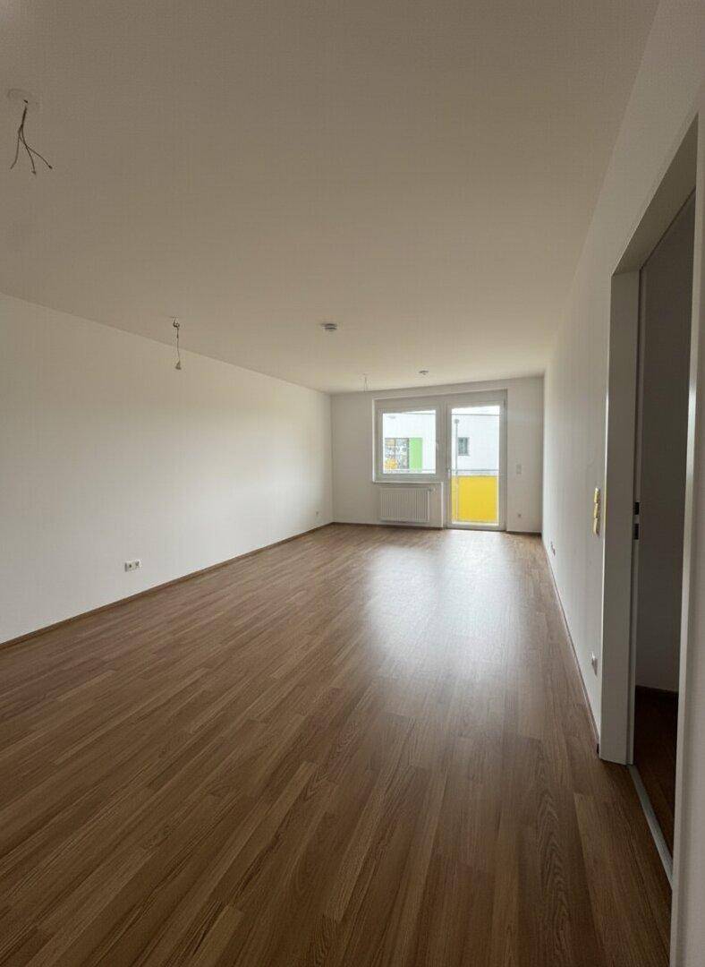 Geräumiges, leeres Wohnzimmer mit Laminatboden und Zugang zu einem Balkon.