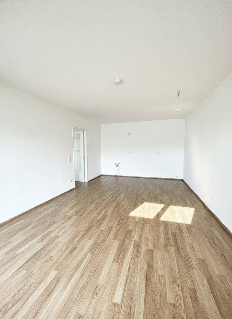 Großzügiges, leeres Wohnzimmer mit Laminatboden und viel Tageslicht.