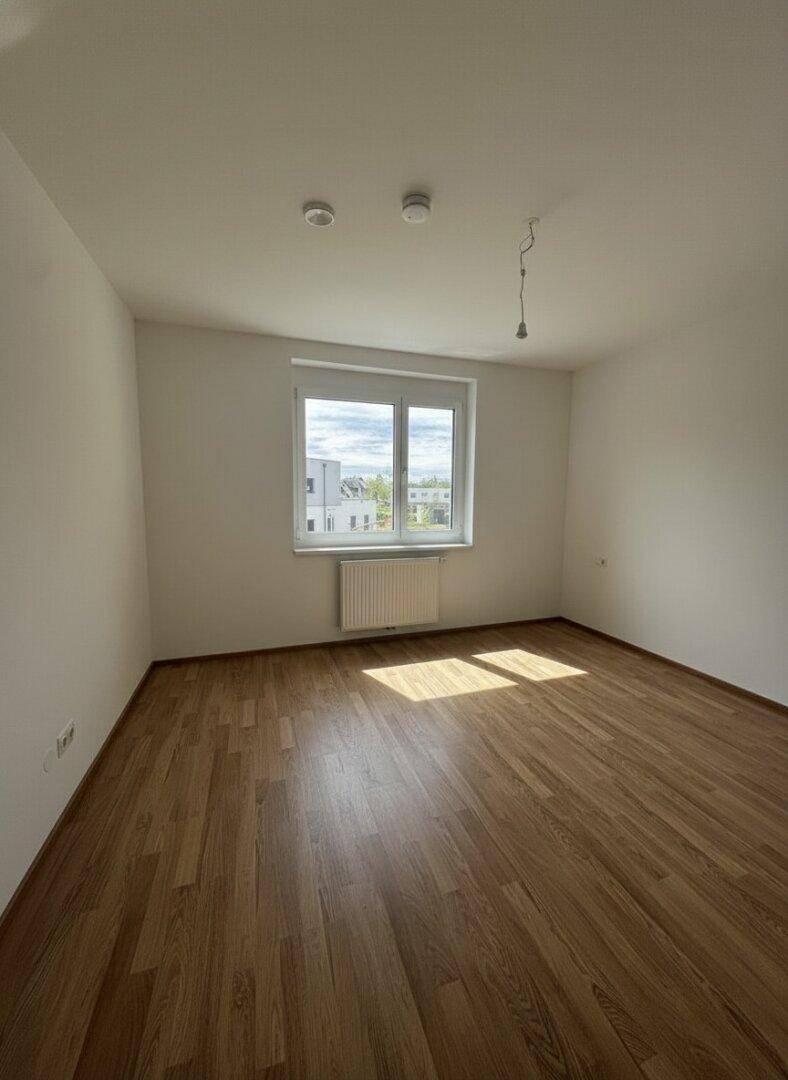 Lichtdurchflutetes Schlafzimmer mit Laminatboden und großem Fenster, das viel Tageslicht hereinlässt.