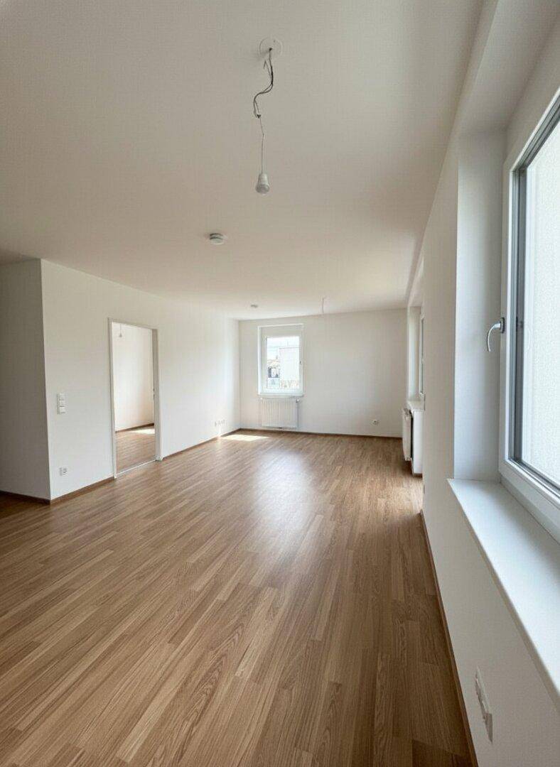 Helles, leeres Wohnzimmer mit großen Fenstern und neuem Laminatboden in einem modernen Apartment.