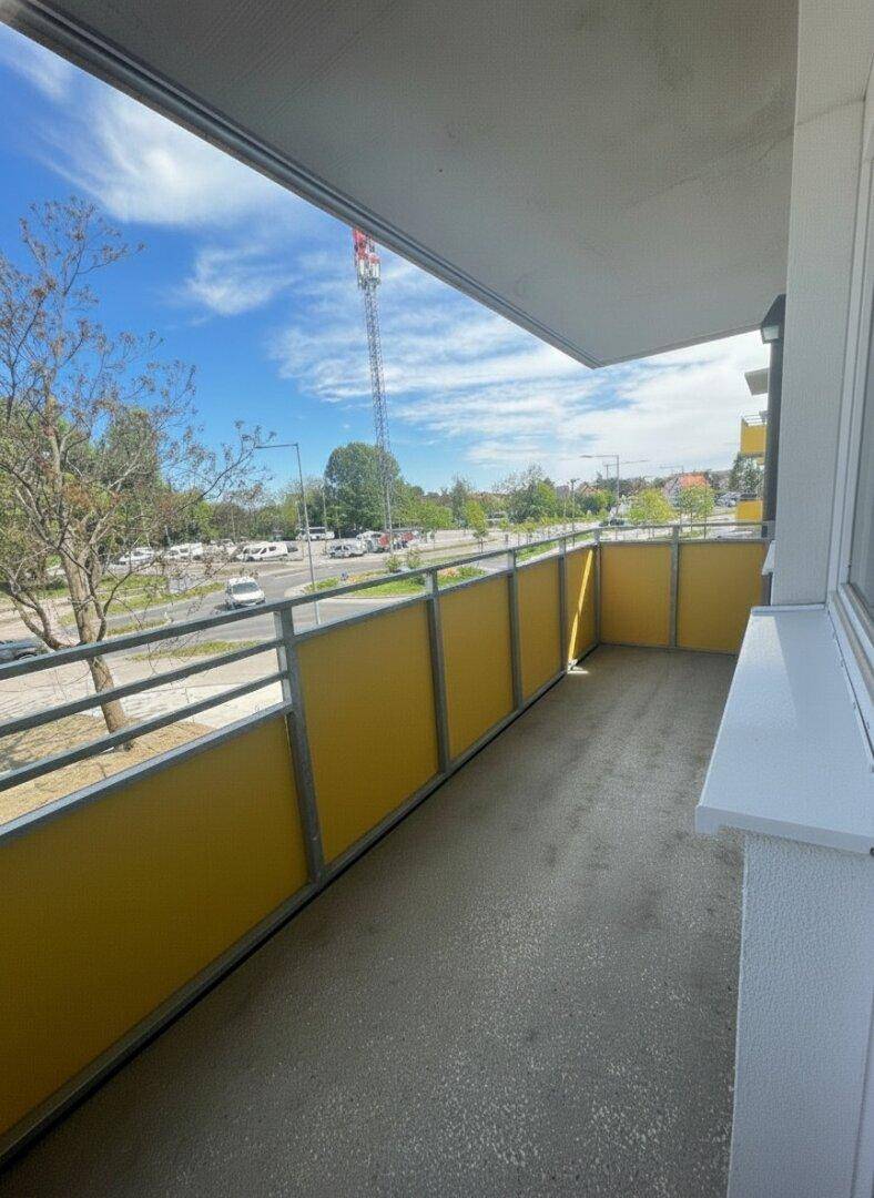 Langer Balkon mit gelben Sichtschutzwänden und Blick auf die Umgebung und einen Sendemast.