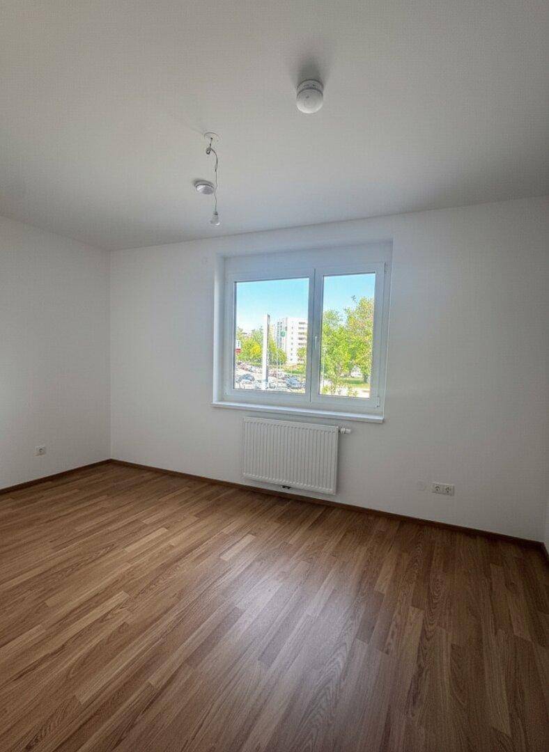 Unmöbliertes Schlafzimmer mit Laminatboden und großem Fenster, das einen Blick nach draußen bietet.