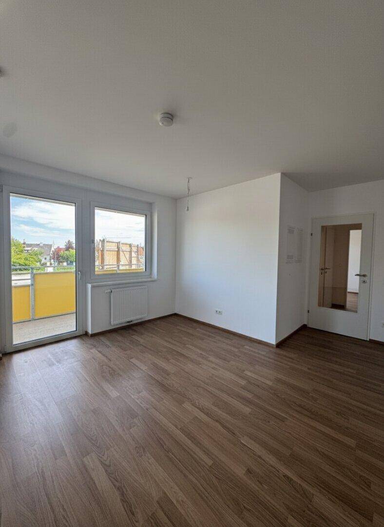 Heller Wohnbereich mit Holzboden und Zugang zum Balkon, bietet viel Tageslicht.
