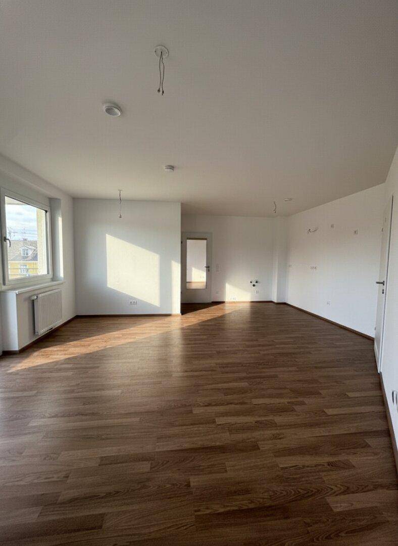 Großzügiger Raum mit Holzboden und viel natürlichem Licht, ideal als Wohnzimmer nutzbar.