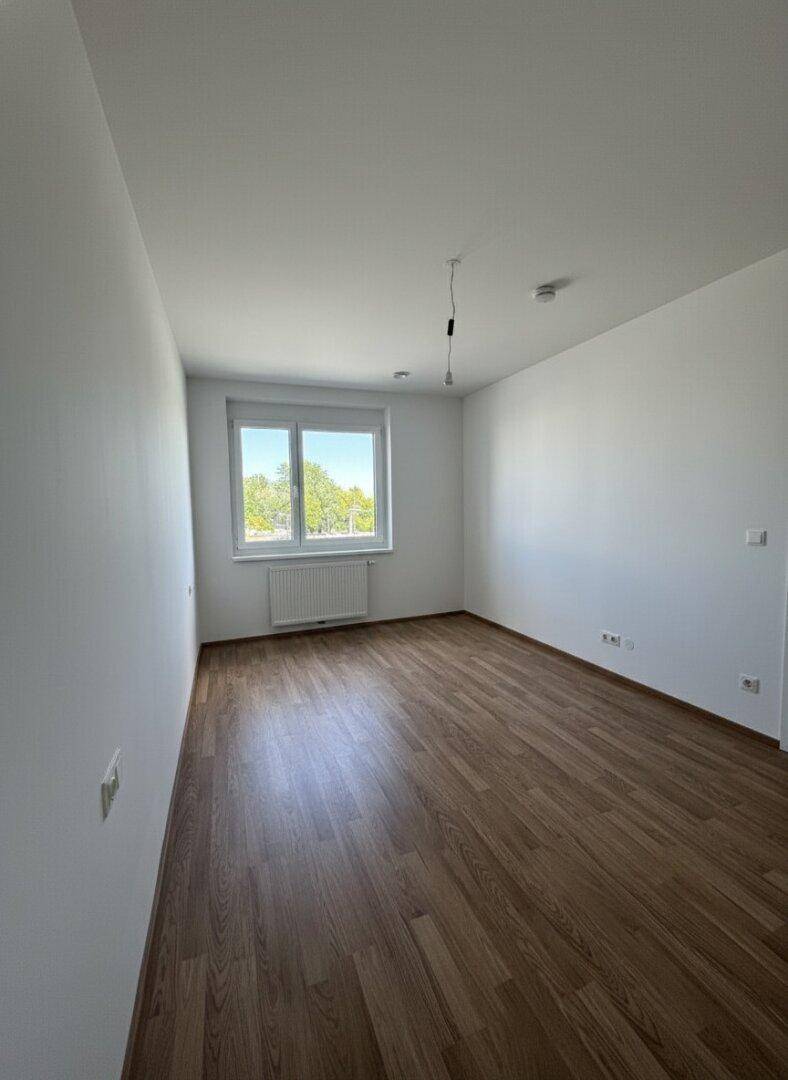 Geräumiges Schlafzimmer mit Laminatboden und viel Tageslicht durch das Fenster.