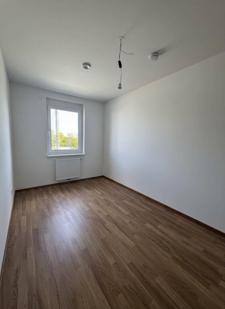 Helles Schlafzimmer mit Laminatboden und einem Fenster, das viel Licht hereinlässt.