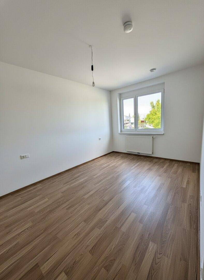 Schlafzimmer mit Laminatboden, weißen Wänden und einem großen Fenster.