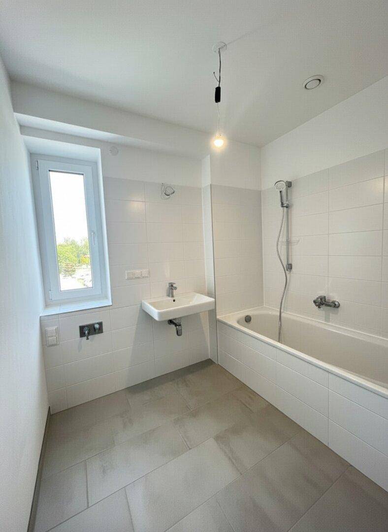 Modernes Badezimmer mit Badewanne, Waschbecken und Fenster für Tageslicht.