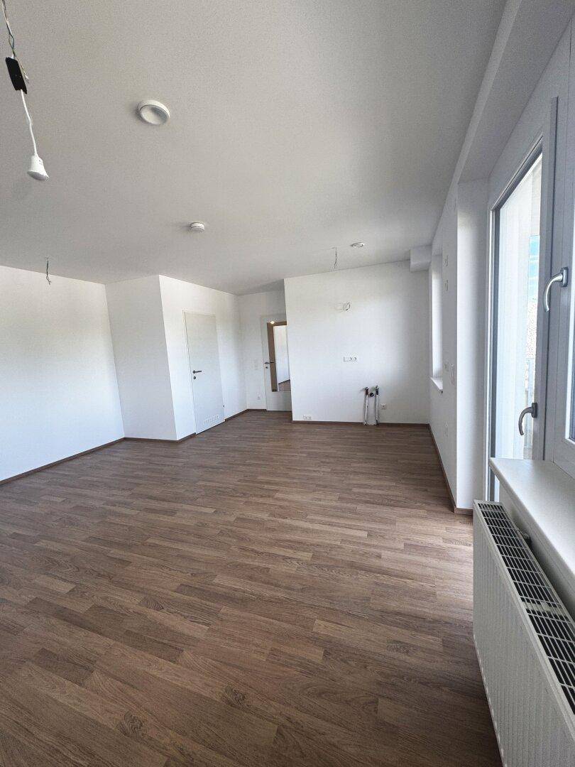Heller, leerer Wohnraum mit neuem Laminatboden und großen Fenstern, bereit zum Einzug.