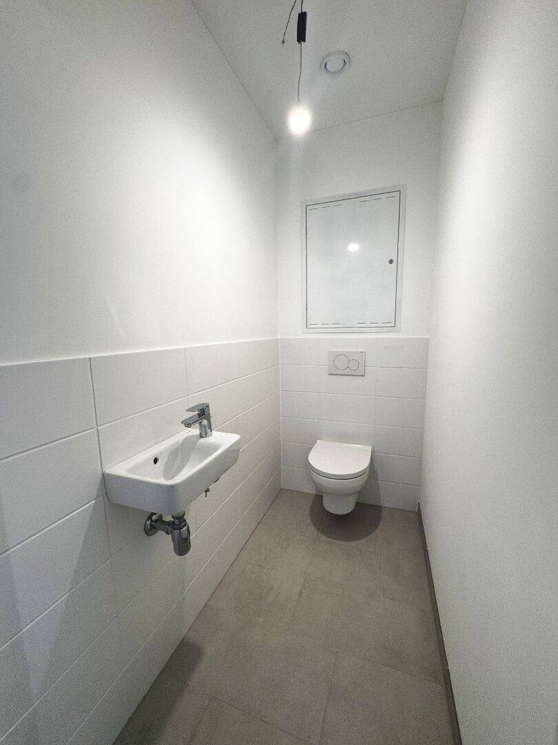 Modernes Gäste-WC mit wandhängendem WC, kleinem Waschbecken und hellen Fliesen.