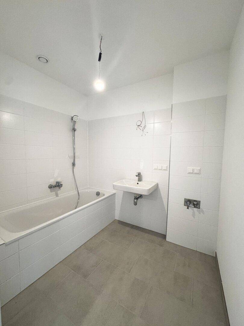 Modernes Badezimmer mit weißen Wandfliesen, grauen Bodenfliesen und einer Badewanne.